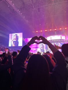 a crowd at a concert with their hands in the shape of a heart and an image of a woman's face