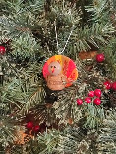 an ornament is hanging on the tree with berries and pine cones around it