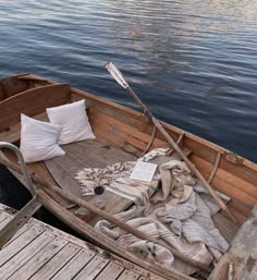 an old wooden boat with pillows and blankets on the front is docked at a pier