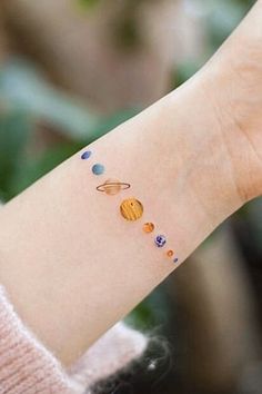 a woman's arm with a small wrist tattoo featuring the solar system on it