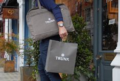 a man carrying two bags in front of a storefront with the word trunk on it