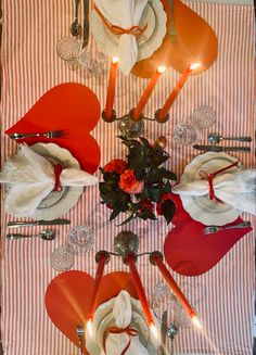 the table is set with red and white plates, silver utensils and flowers