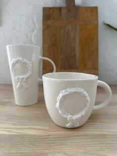 two white coffee cups sitting on top of a wooden table