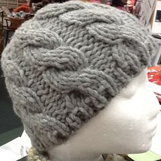 a gray knitted hat on display in a store window with people looking at it