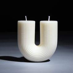 two white candles sitting next to each other on top of a black surface with the letter u in front of them