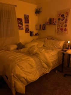 an unmade bed in a dimly lit room with pictures on the wall above it