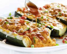 someone is drizzling sauce on zucchini slices with cheese and other toppings