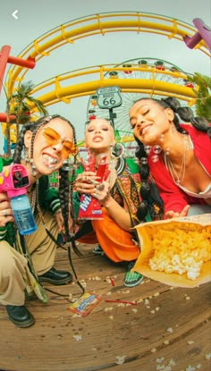 three women taking pictures with their cell phones while sitting on the ground at an amusement park