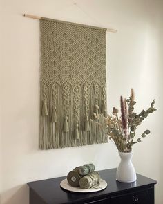 a white vase filled with flowers on top of a black dresser next to a wall hanging