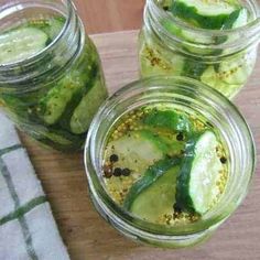 three jars filled with pickled cucumbers on top of a wooden cutting board