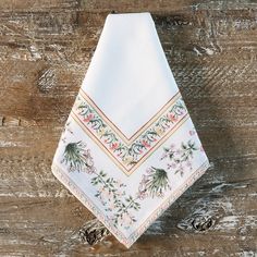 a white napkin with floral designs on it sitting on top of a wooden table next to pine cones