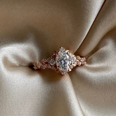 an engagement ring is sitting on top of a satin fabric, with the diamond set in the center