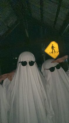 three people in white ghost costumes with black sunglasses and one wearing a yellow crossing sign