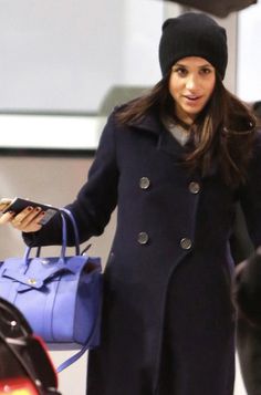 a woman in a black hat and coat carrying a blue handbag