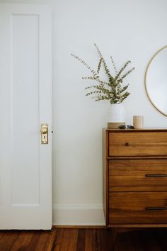 a wooden dresser with a mirror on top of it and a plant in the corner