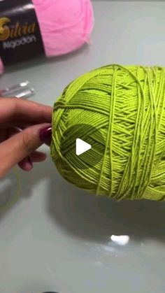 a ball of yarn is being held up by someone's hand while they are knitting