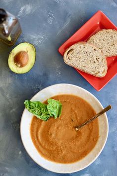 a bowl of soup with bread and an avocado