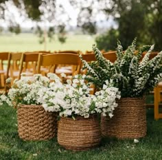 several baskets with flowers are lined up on the grass in front of rows of chairs