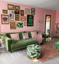 a living room with pink walls, green couches and various framed pictures on the wall