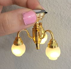 a person with pink nail polish on their fingers holding a gold chandelier light