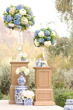 two blue and white vases with flowers in them sitting on a table next to each other