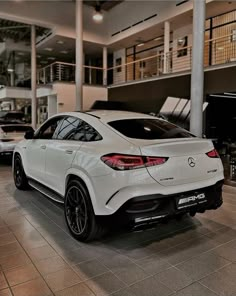 the rear end of a white mercedes suv parked in a showroom with other cars