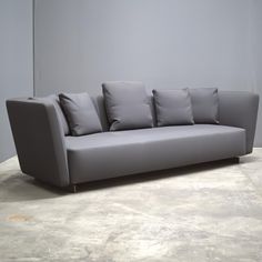 a gray couch sitting on top of a cement floor next to a white wall with lots of pillows