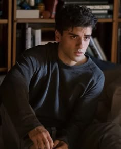 a young man sitting on top of a couch next to a book shelf