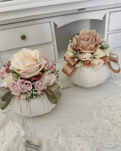 two white pumpkins decorated with flowers on a lace tablecloth and some other decorations