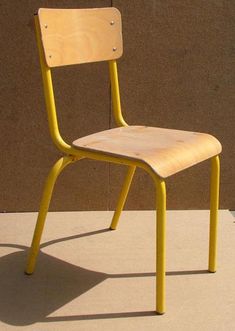 a yellow chair sitting on top of a cement floor next to a wall with a brown building in the background