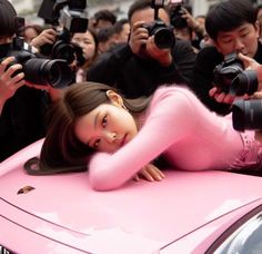 a woman laying on top of a pink car surrounded by photographers