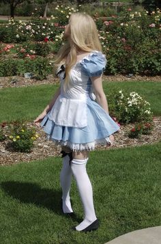 a woman in a blue dress and white stockings is standing on the grass with her back to the camera