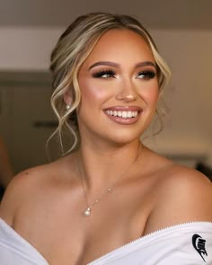 a woman with blonde hair wearing a white top and diamond necklace smiling at the camera