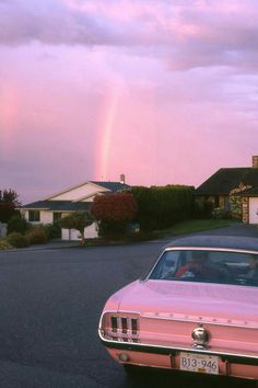 a pink car is parked in front of a house with a rainbow in the background