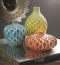 three different colored vases sitting on top of a metal table in front of a mirror