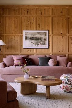 a living room with wood paneling and pink couches in front of a coffee table