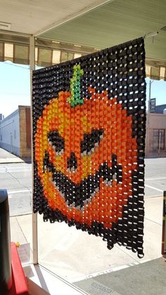 an orange and black pumpkin made out of plastic bottle caps hanging from a metal pole