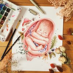 a drawing of a baby wrapped in a blanket on top of a table next to watercolor paints