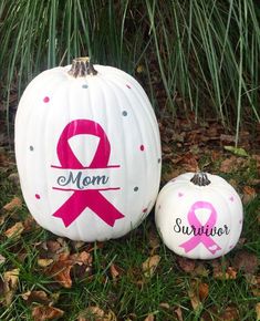 two white pumpkins with pink ribbon on them sitting in the grass next to some leaves