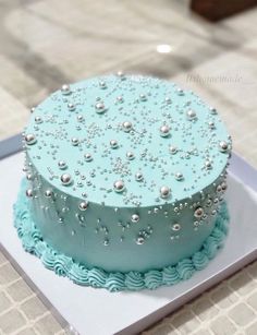 a blue and white cake with pearls on it sitting on top of a table next to a plate