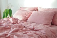 a bed with pink sheets and pillows on top of it, next to a potted plant