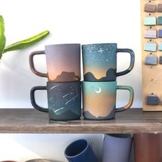 four coffee mugs sitting on top of a wooden shelf next to a succulent plant