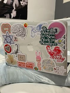 an open laptop computer sitting on top of a white bed covered in stickers and decals