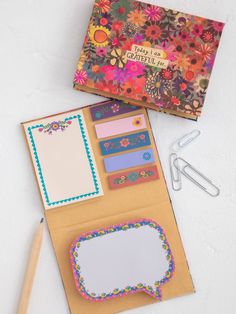 an open notebook with flowers on it next to some paper clips and a pair of scissors