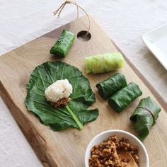 a wooden cutting board topped with green leafy vegetables next to a bowl of food