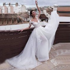 a woman in a white dress standing on top of a roof with her arms outstretched