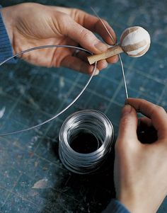 two hands are holding scissors and threading together some wire to make a ball ornament