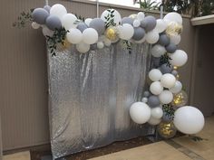 the balloon arch is decorated with silver and white balloons, greenery and gold confetti