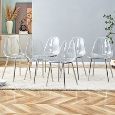 four clear chairs sitting on top of a wooden floor next to a white rug in a living room