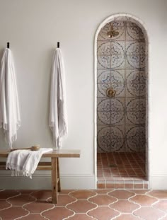 two white towels hanging on the wall next to a wooden bench with an open door